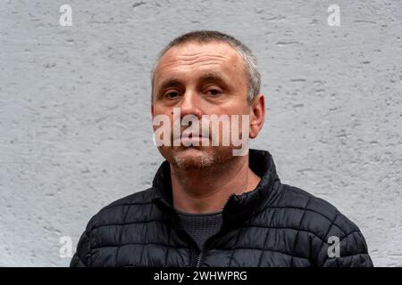 Ein grauhaariger älterer Mann, 45-50 Jahre alt, an einer hellen Wand, der eine schwarze Jacke trägt, schaut in die Kamera. Stockfoto