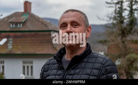 Grauhaariger Mann 45-50 Jahre alt in einer Jacke im Hintergrund eines Landhauses. Stockfoto