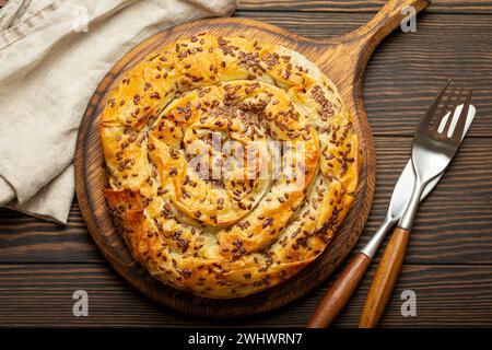 Bürek aus Phyllo-Teig mit Füllung auf Schneidebrett, dunkelbrauner rustikaler Holzhintergrund von oben. Traditionelles herzhaftes spir Stockfoto