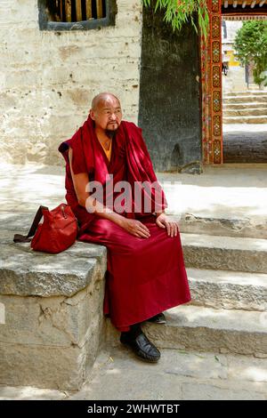 Ein älterer buddhistischer Mönch ruht auf der Steintreppe des Klosters Sera in Lhasa. Stockfoto