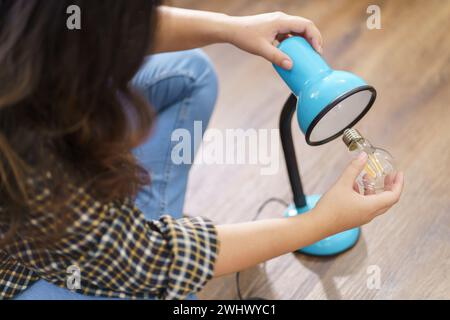 Asiatische Frau wechselt Glühbirne in der Lampenrenovierung mit Ausrüstung zum selbermachen der Glühbirne und Lampe, die auf dem Boden sitzt Stockfoto