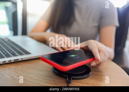 Laden des Mobiltelefonakkus mit dem drahtlosen Gerät in der Tabelle. Smartphone wird auf einem Ladepad aufgeladen. Mobiltelefon in der Nähe des Kabelnetzes Stockfoto