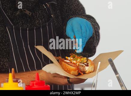 Mitte des Körpers des Küchenchefs, der Hotdog für einen Kunden am Stand mit frischen Hotdogs auf dem Naplavka Street Food Farmers Market in Prag, Tschechisch, zubereitet. Stockfoto