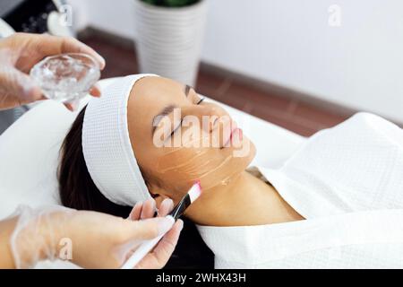 Der Schönheitsmeister wendet eine verjüngende Maske auf das Gesicht des Kunden an. Stockfoto