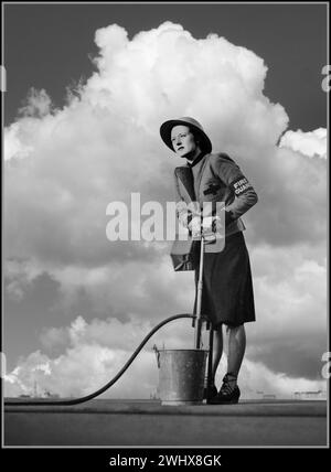 1941 WW2 weibliche Feuerwache in Uniform Propagandabild Frauen in Kriegsarbeit Großbritannien mit einer Steigbügelpumpe im Brandfall, auf dem Dach des Gebäudes in LONDON Großbritannien 2. Weltkrieg Eine weibliche Feuerwache demonstriert Steigbügelpumpe auf dem Dach des Londoner Gebäudes, Sie trägt ihr Feuerwehrarmband, einen Stahlhelm und trägt ihre Gasmaske. Stockfoto