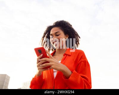 Sorglose junge afroamerikanische Frau, die in einer Stadt mit dem Handy chatten Stockfoto