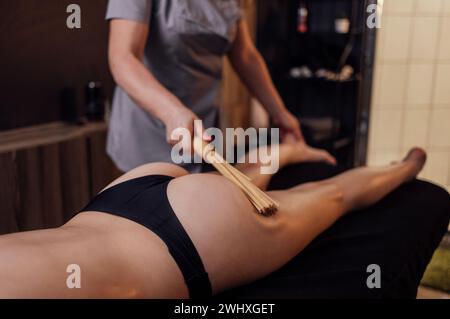 Die Masseurin nimmt im Spa-Salon eine Anti-Cellulite-Massage mit Bambusstäben vor. Beinmassage mit Bambusbesen im Schönheitszentrum oder Stockfoto