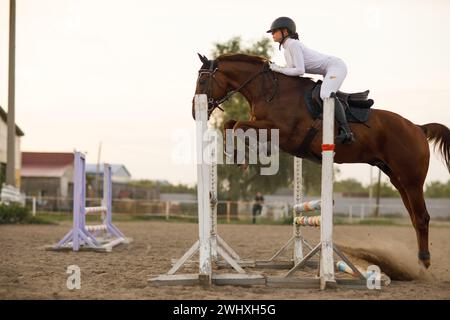 Seitenansicht eines Dressurpferdes im Gurtzeug mit Reiterjockey in Helm und weißer Uniform beim Springreiten. Stockfoto