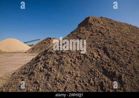 Haufen von feinem braunem und braunem Sand und Stapelförderer in kommerzieller Sandgrube. Stockfoto