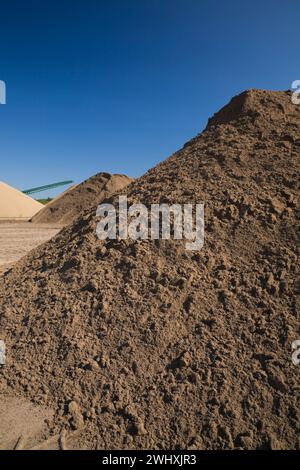 Haufen von feinem braunem und braunem Sand und Stapelförderer in kommerzieller Sandgrube. Stockfoto