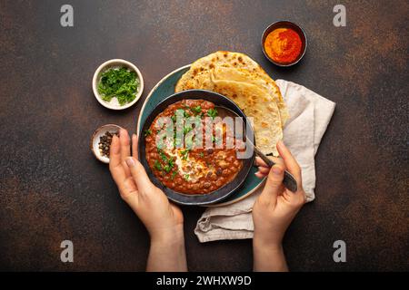 Weibliche Hände halten eine Schüssel und essen traditionelles indisches Punjabi-Gericht Dal Makhani mit Linsen und Bohnen serviert mit Naan Flat Stockfoto