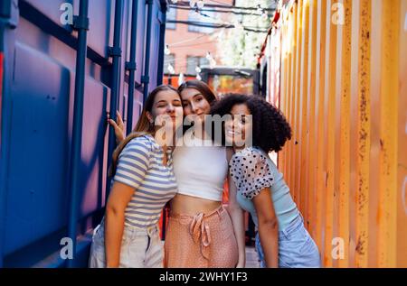 Drei süße Teenager-Mädchen in lässiger Kleidung auf bunten Versandbehältern. Stockfoto