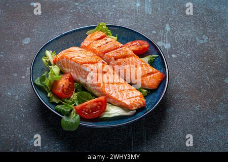 Gegrilltes Fisch Lachssteak mit Gemüsesalat auf Keramikplatte auf rustikalem Stein Hintergrund Winkelansicht, ausgewogene Ernährung, gesund n Stockfoto