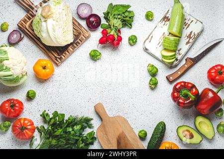 Frisches Gemüse, Schneidebretter aus Holz und Messer auf weißem Küchentisch mit Blick von oben. Kochen vegetarisches Essen von gesund Stockfoto