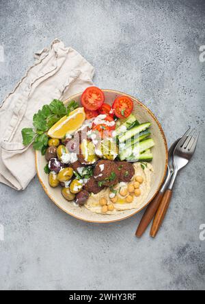 Falafel Salatschüssel mit Hummus, Gemüse, Oliven und Kräutern. Veganer Mittagstisch mit Blick von oben, rustikaler Steinhintergrund, gesunde Mahlzeit Stockfoto