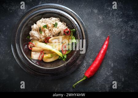 Asiatisches Gericht aus Reis ad Pak Choi (Chinakohl) und roter Chilischote in einer schwarzen Keramikschale mit Knoblauch, Ingwer und Kräutern Stockfoto