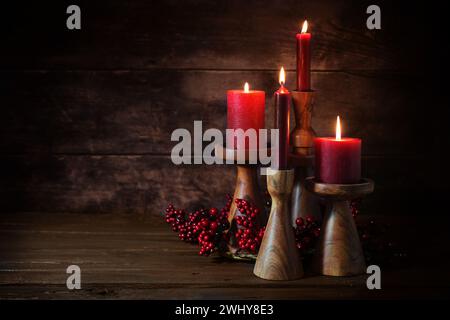 Gruppe von vier roten Kerzen in Kerzenstöcken aus Holz als Adventsdekoration vor dunklem rustikalem Holzhintergrund, Feiertagshuhn Stockfoto