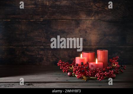 Zweiter Adventstag mit zwei roten Kerzen in einem Kranz aus Beeren mit Weihnachtsdekoration vor dunklem rustikalem Holzhintergrund Stockfoto