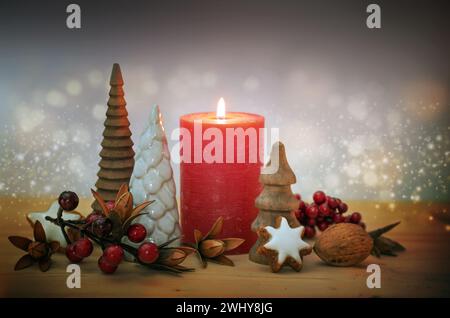 Weihnachtsdekoration mit einer roten Kerze, kleinen künstlichen Tannen, Beeren und Zimtstern-Kekse gegen ein funkelndes Bokeh Stockfoto