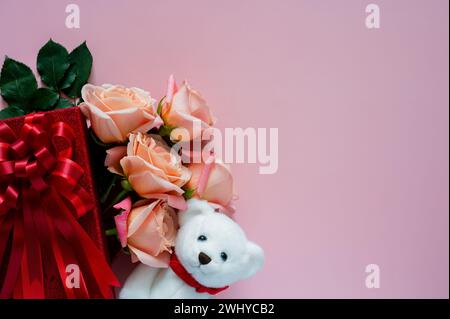 Rosafarbene Rosen in roter Geschenkbox mit weißer Teddybärpuppe auf rosa Hintergrund für Valentinstag-Konzept. Stockfoto