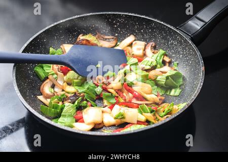 Gebratenes Gemüse in einer Pfanne, gesunde vegetarische Küche mit Zutaten wie Paprika, Pilze, Zwiebeln und Gemüse Stockfoto