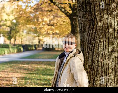 Reife, lächelnde Frau im Herbstpark am Baum Stockfoto