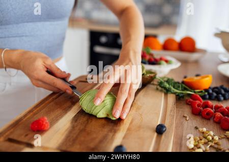 Eine attraktive süße asiatische Frau lächelt und kocht das Frühstück in der Küche. Eine junge charmante Koreanerin lacht und schneidet Vegetabl Stockfoto