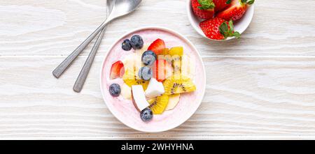 Gesundes Frühstück oder Dessert Joghurtschale mit frischer Banane, Erdbeere, Heidelbeere, kokos, Kiwi-Draufsicht, rustikales weißes Holz-bac Stockfoto