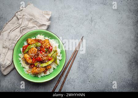 Asiatisches süß-saures Hähnchen mit Gemüse, gebraten und Reis in Keramikschale mit Essstäbchen von oben auf graue rustikale Str. Stockfoto