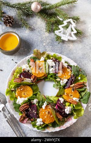 Vorspeise zu Weihnachten. Weihnachtskranzsalat mit Roter Bete, Mandarinen, Fetakäse und Pekannüssen auf dem festlichen Tisch. Stockfoto