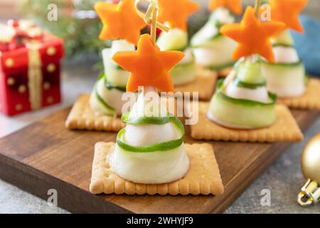 Kreative Vorspeisen weihnachten. Weihnachtsbäume aus Schinken, Gurke, Käse und Karottenstern auf Crackern auf dem festlichen Tisch. Stockfoto