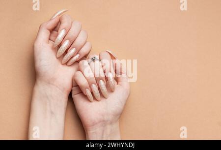 Weibliche Hände auf braunem Hintergrund und wunderschöne Perlenmaniküre. Stockfoto