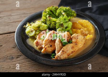 Hähnchenfilet in Orangensauce mit Brokkoli-Lauch-Gemüse auf einem schwarzen Teller auf dunklem rustikalem Holz, Low Carb Diät-Gericht, Kopie Spac Stockfoto