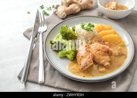 Gebratenes Hähnchenfilet in Orangen-Ingwersauce mit Brokkoli-Gemüse und Reis, serviert auf einem Teller mit Besteck und Serviette auf einem wh Stockfoto