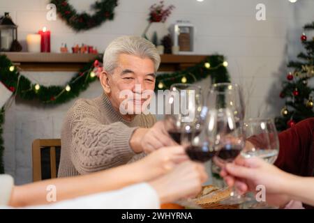 Glückliche asiatische Familie, die zu Hause Weihnachten feiert. Fröhliche Senioreneltern und Kinder im Weihnachtsmann-Hut, der Gläser anklickt Stockfoto