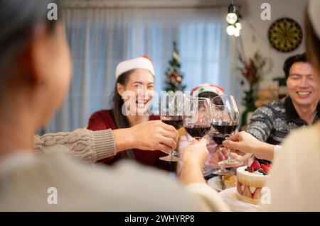 Glückliche asiatische Familie, die zu Hause Weihnachten feiert. Fröhliche Senioreneltern und Kinder im Weihnachtsmann-Hut, der Gläser anklickt Stockfoto