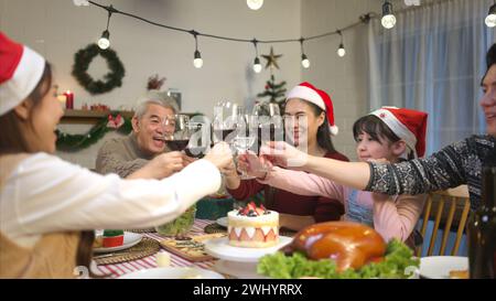 Glückliche asiatische Familie, die zu Hause Weihnachten feiert. Fröhliche Senioreneltern und Kinder im Weihnachtsmann-Hut, der Gläser anklickt Stockfoto