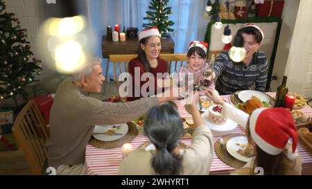 Glückliche asiatische Familie, die zu Hause Weihnachten feiert. Fröhliche Senioreneltern und Kinder im Weihnachtsmann-Hut, der Gläser anklickt Stockfoto