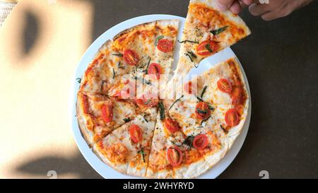 Die Hand nimmt ein Stück von frisch gebackener Margherita Pizza Stockfoto