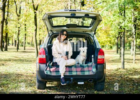 Junge Frau mit Hund, der sich entspannt und die Natur genießt, sitzt im Kofferraum Stockfoto