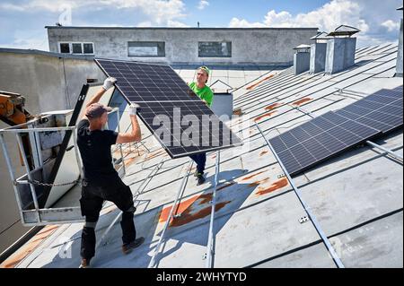 Arbeiter, die Solarpaneele auf dem Metalldach des Hauses mit Hilfe eines Kranaufzugs bauen. Zwei Monteure tragen Photovoltaik-Solarmodul im Freien. Konzept der Erzeugung erneuerbarer Energien. Stockfoto