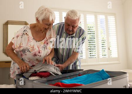 Glückliches kaukasisches Seniorenpaar, das Koffer im sonnigen Schlafzimmer zu Hause packt Stockfoto