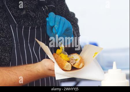 Mitte des Körpers des Küchenchefs, der Hotdog für einen Kunden am Stand mit frischen Hotdogs auf dem Naplavka Street Food Farmers Market in Prag, Tschechisch, zubereitet. Stockfoto