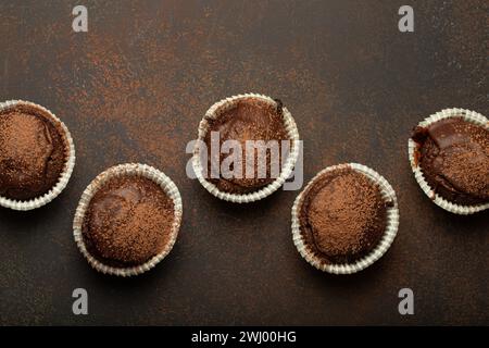 Schokolade und Kakao bräunliche Muffins von oben auf braunem rustikalem Steinhintergrund, süße hausgemachte Cupcakes aus dunkler Schokolade Stockfoto