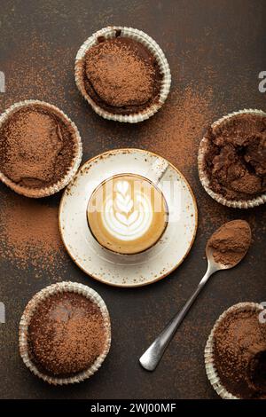 Schokolade und Kakao bräunliche Muffins mit Kaffee Cappuccino in der Tasse von oben Blick auf braunen rustikalen Stein Hintergrund, süße hausgemachte dunkle Stockfoto