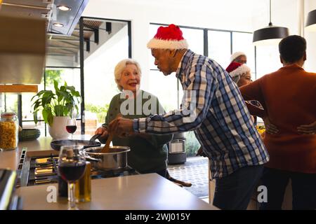 Glückliche, vielfältige Freunde, die sich mit weihnachtsmann-Hut in der sonnigen Küche zuhause zubereiten Stockfoto