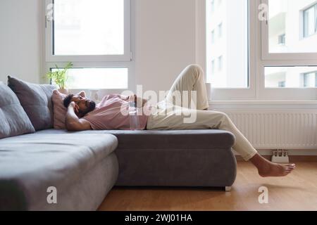 Junger Mann, der nach dem Heimtraining, der Meditation zu Hause, dem morgendlichen oder abendlichen Workout auf dem Sofa liegt. Stockfoto