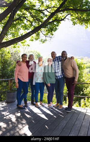 Glückliche, vielfältige Gruppe von Senioren, die sich umarmen und im sonnigen Garten lächeln Stockfoto