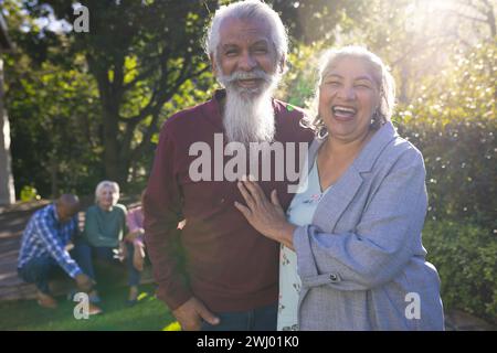 Glückliches birassisches Paar älterer Freunde, die sich umarmen und im sonnigen Garten lächeln Stockfoto