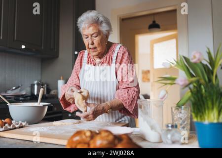 Seniorin, die traditionelle ostermahlzeiten für die Familie zubereitet, Teig für osterbrötchen kneten. Nachbildung von Familienrezepten, individuell. Stockfoto